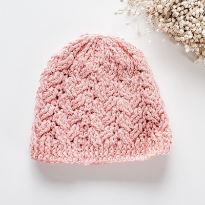 Touca cor-de-rosa tricotada com padrão em relevo e raminhos secos ao lado