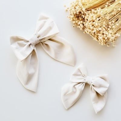 Dois laços de tecido bege claros e um raminho de flores secas sobre um fundo branco