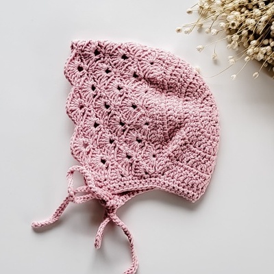Gorro de bebé de croché rosa com laços e flores secas ao lado
