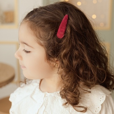 Menina com mola de cabelo vermelha e camisa branca com gola grande bordada em ambiente interior