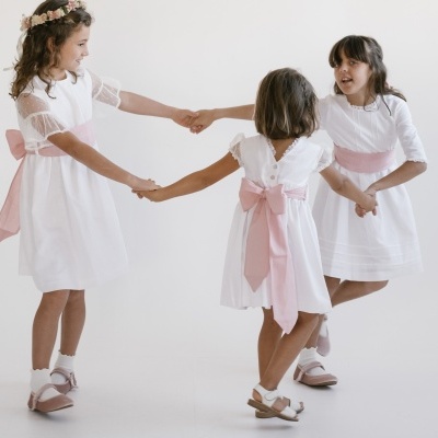 Três meninas com vestidos brancos e laços rosa a brincar num fundo branco