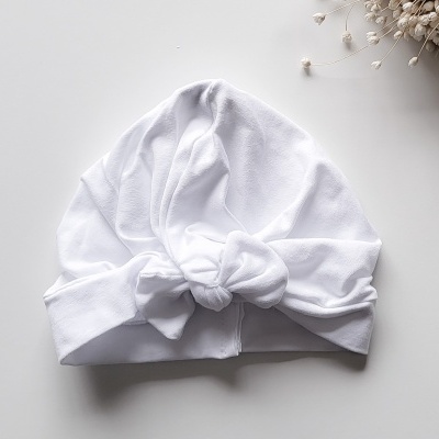Touca branca de tecido macio com nó frontal sobre superfície branca