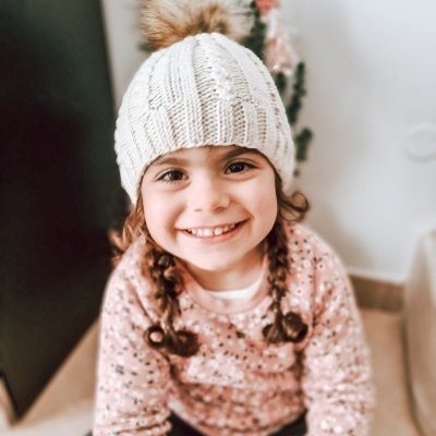 Criança com gorro branco de malha sentada e sorridente, com camisola rosa de flores