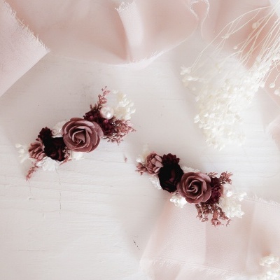 Acessórios de cabelo florais rosa e vinho sobre superfície branca com tecido rosa