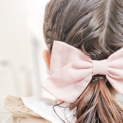 Laço de cabelo rosa claro em criança com roupa bege e branca.