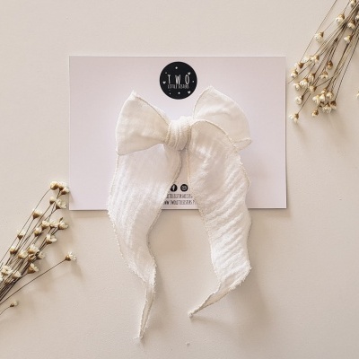 Laço branco em tecido com textura ondulada num cartão branco com logótipo TMO BOWS em superfície clara