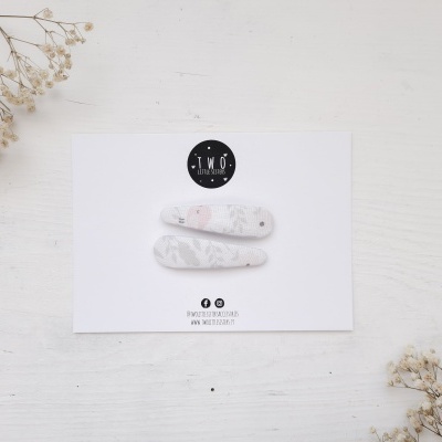 Par de molas de cabelo brancas com padrão cinza num cartão branco com logo TMQ