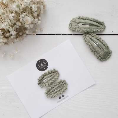 Presilhas de cabelo verdes felpudas sobre cartão e superfície branca com ramo de flores secas