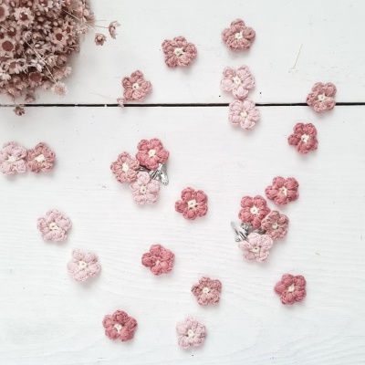 Flores pequenas de croché em tons rosa sobre superfície branca de madeira