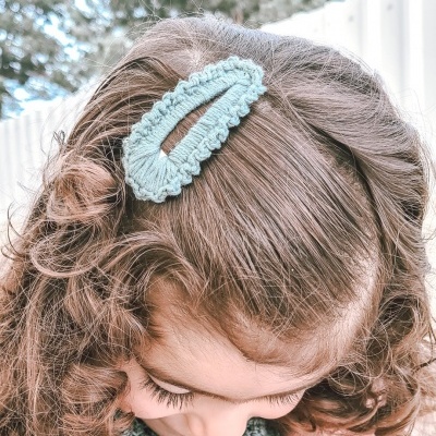 Presilha azul de crochê num cabelo cacheado de criança com suéter rosa e golinha azul ao ar livre