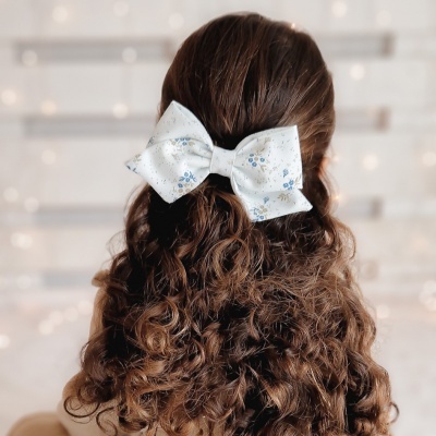 Laço de cabelo branco com padrão floral em cabelo cacheado castanho visto de trás