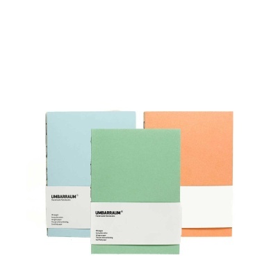 Três cadernos artesanais coloridos com faixa branca e texto preto