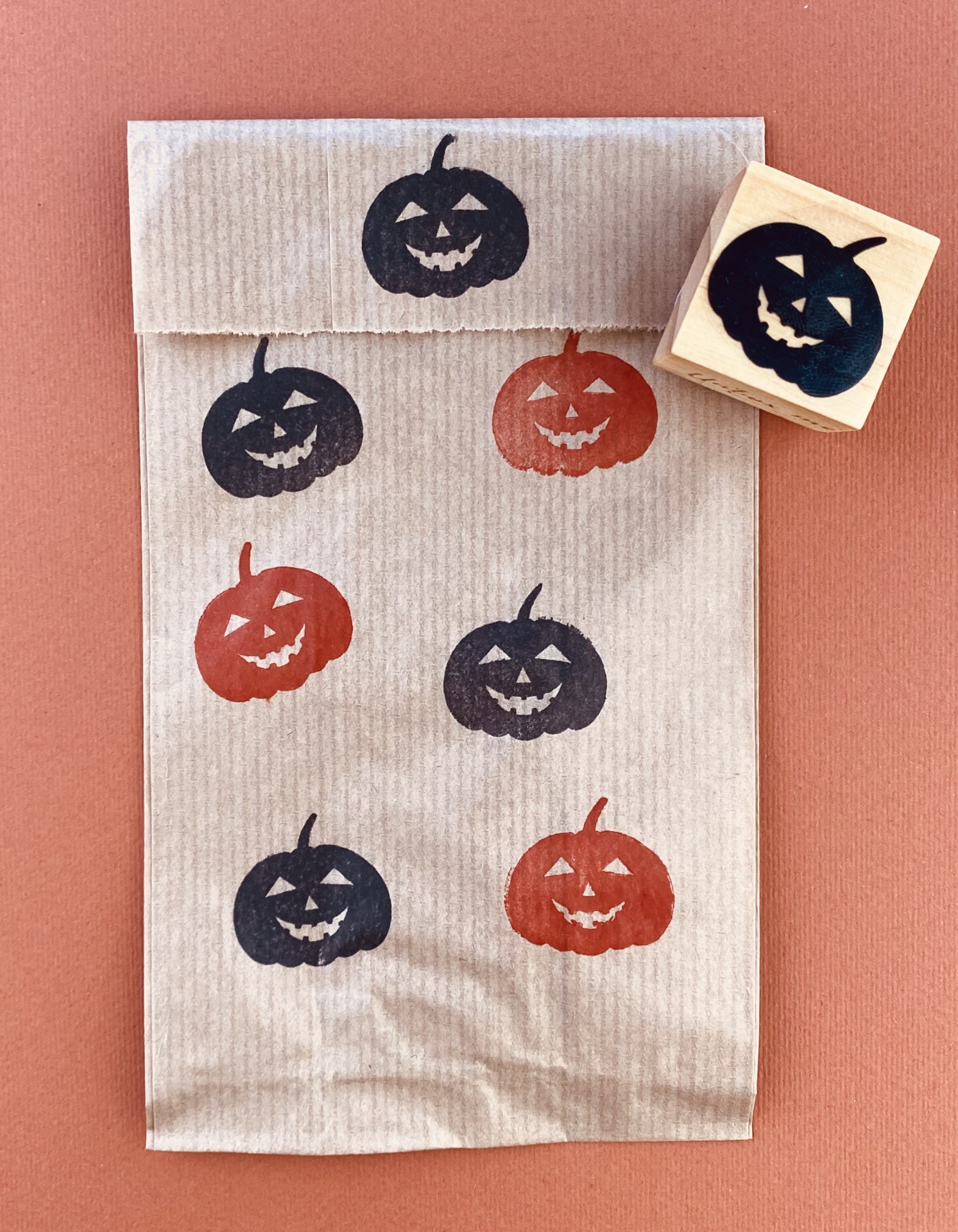 Saco de papel castanho com abóboras de Halloween carimbadas e carimbo quadrado com abóbora preta