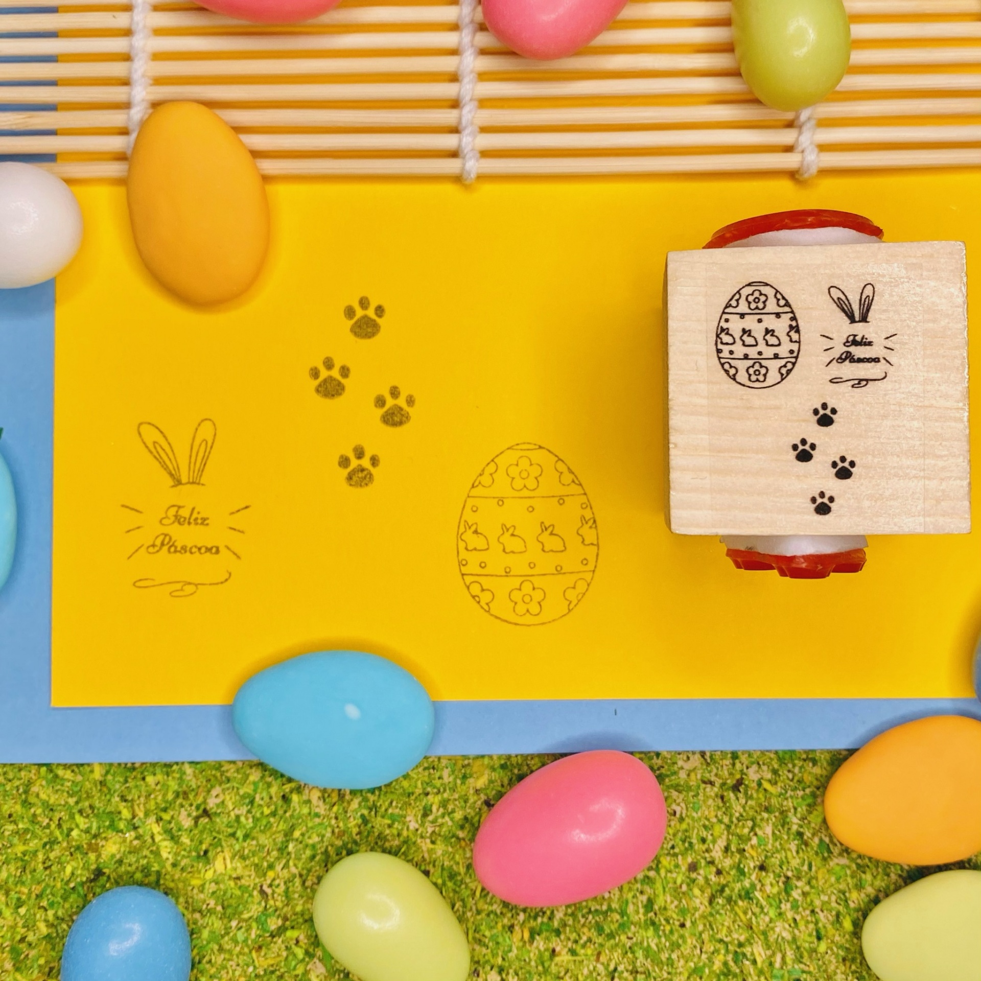 Carimbo de madeira com desenho de ovo de Páscoa, coelho e pegadas, com amêndoas coloridas ao redor