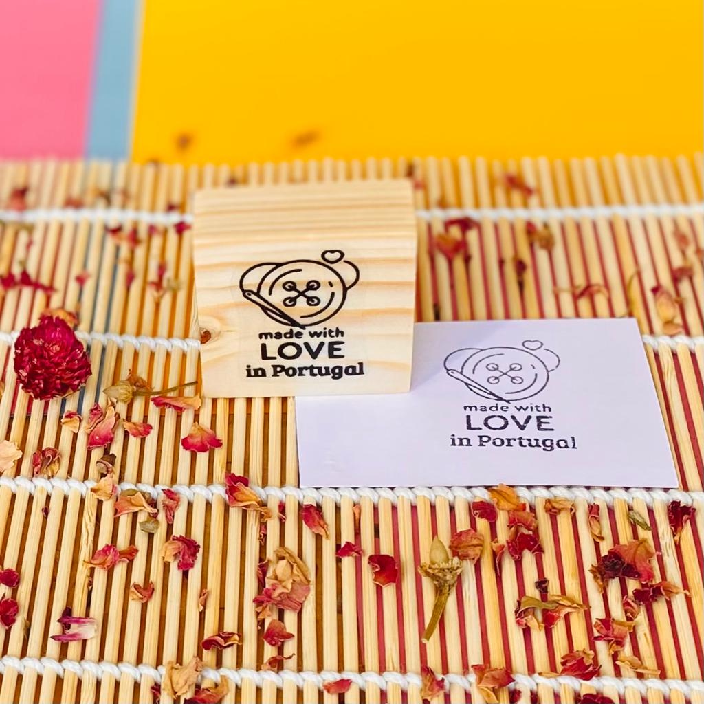 Selo de madeira quadrado com gravura e papel com desenho semelhante sobre tapete de junco e flores secas