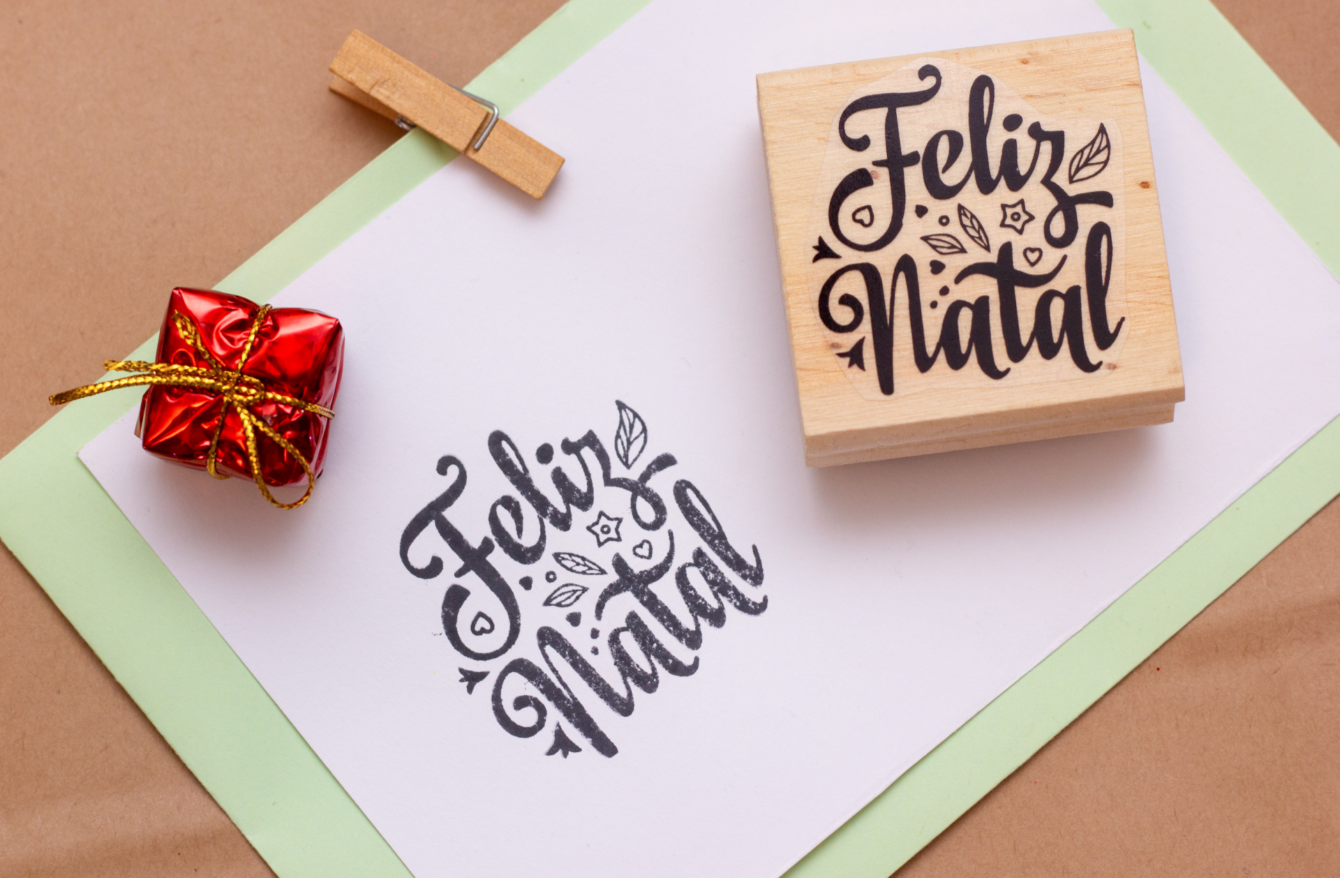 Carimbo de madeira com 'Feliz Natal' e um presente pequeno vermelho sobre mesa