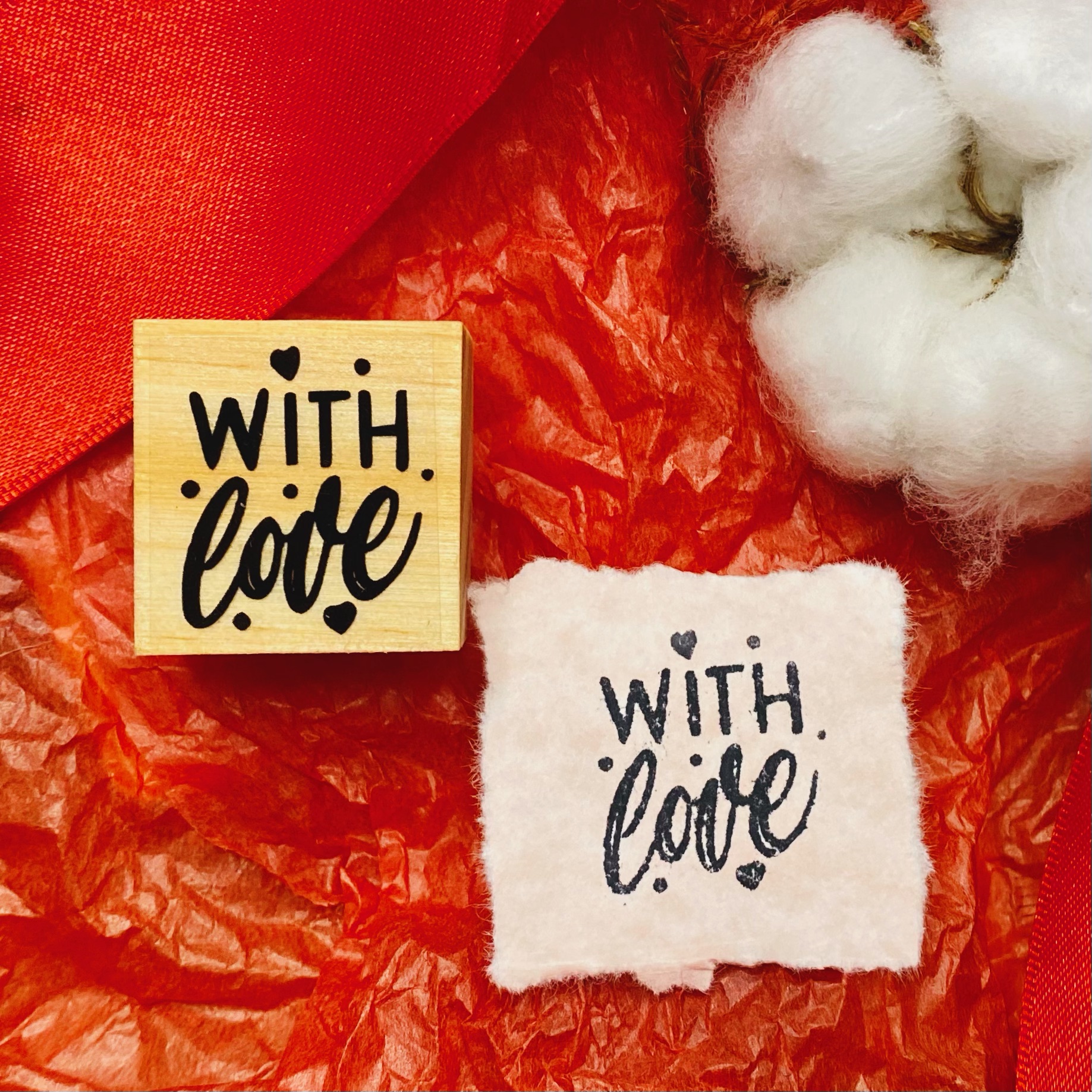 Carimbo de madeira com frase 'WITH love' e impressão em papel branco, algodão e fundo vermelho