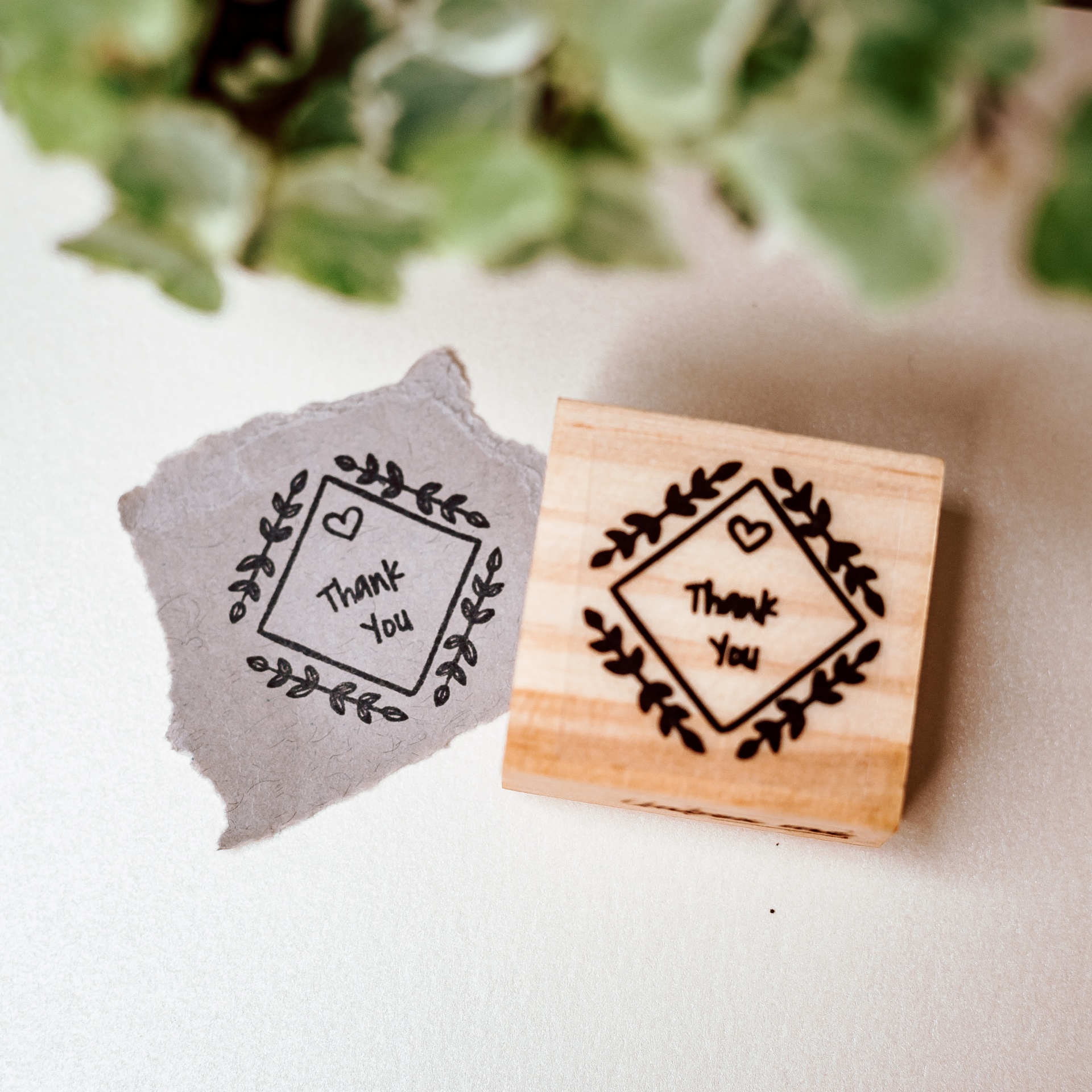 Carimbo de madeira com texto 'Thank You' e desenho decorativo ao lado da impressão em papel cinza
