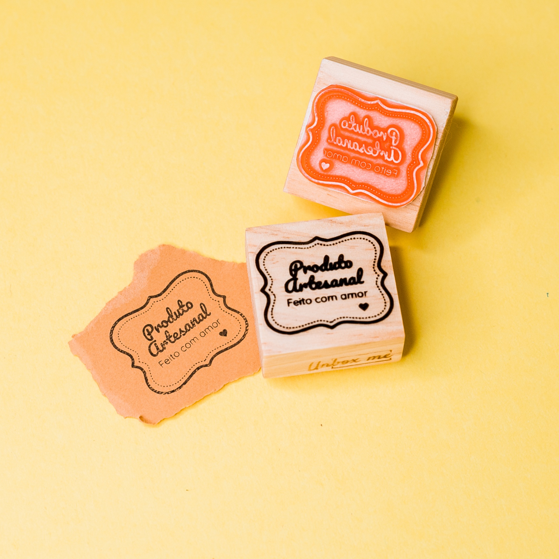Dois carimbos de madeira para artesanato e papel com carimbo aplicado sobre fundo amarelo