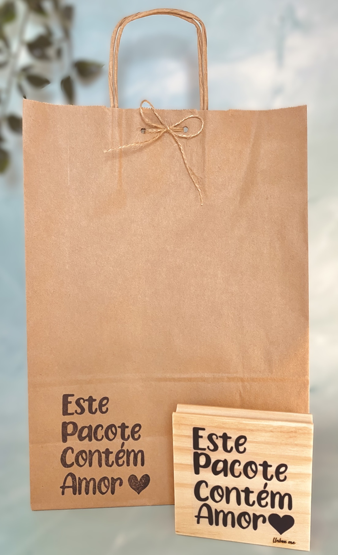 Saco de papel castanho com alças e laço, e frase Este Pacote Contém Amor, com placa de madeira com a mesma frase