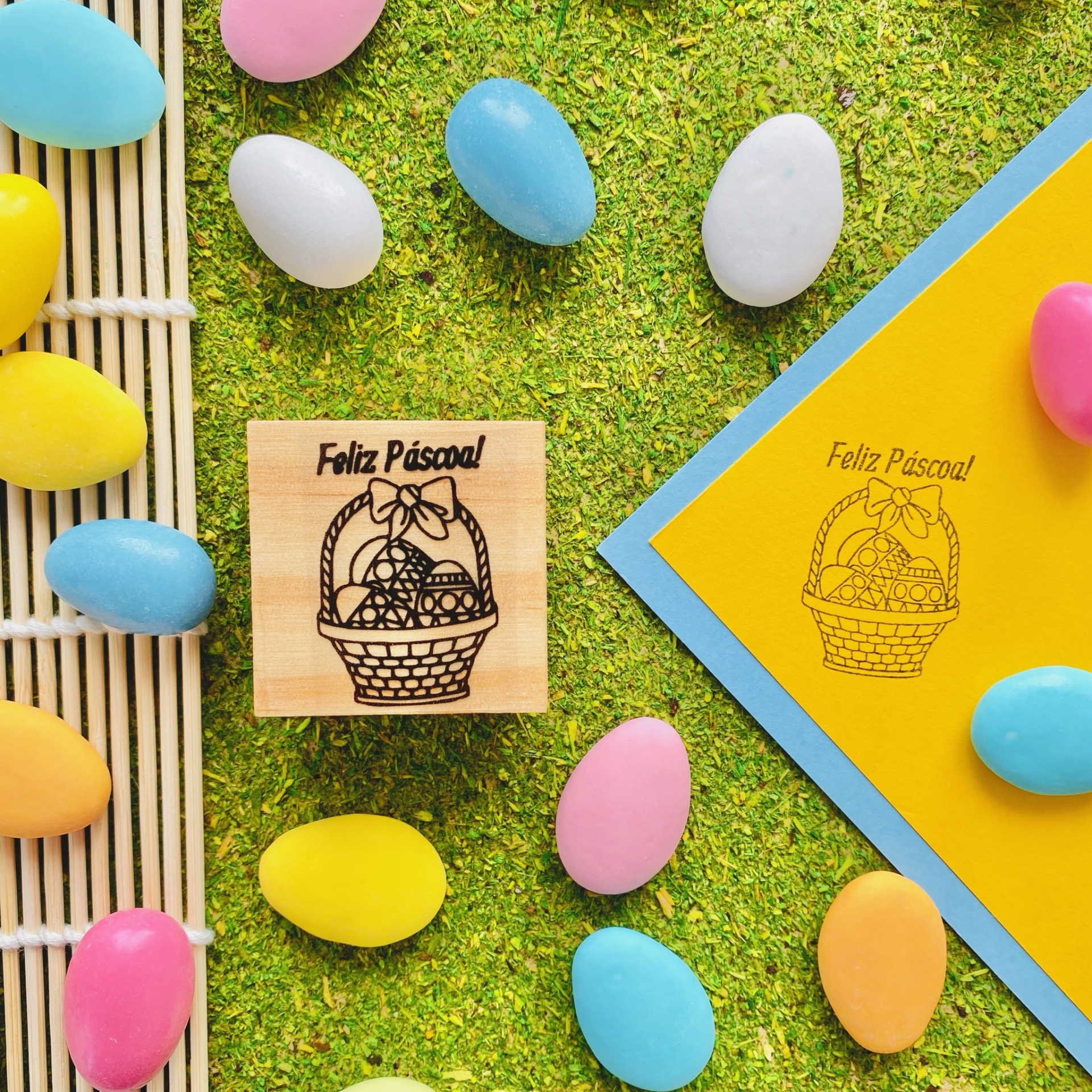 Carimbo de madeira com cesta de Páscoa e ovos coloridos em fundo de relva sintética