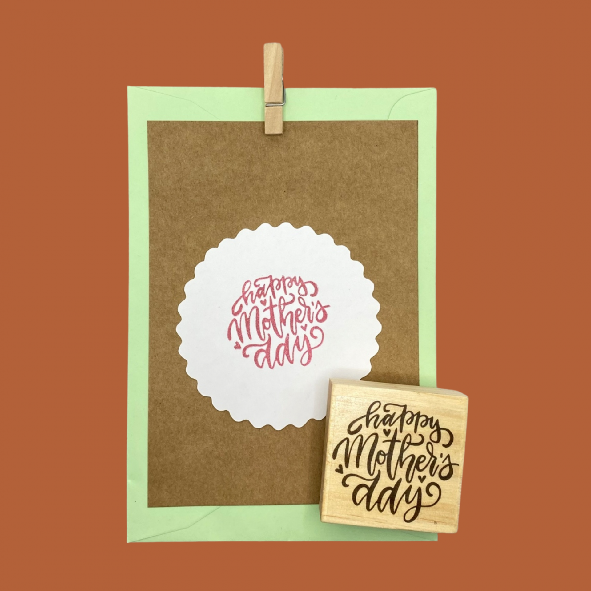 Cartão castanho com selo branco e envelope verde claro com mensagem 'happy Mother's day' e carimbo de madeira