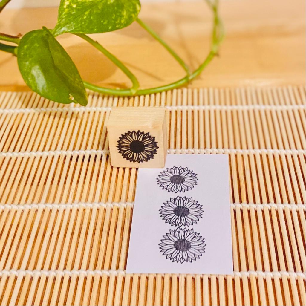 Carimbo de madeira com desenho de girassol e papel com impressões do carimbo