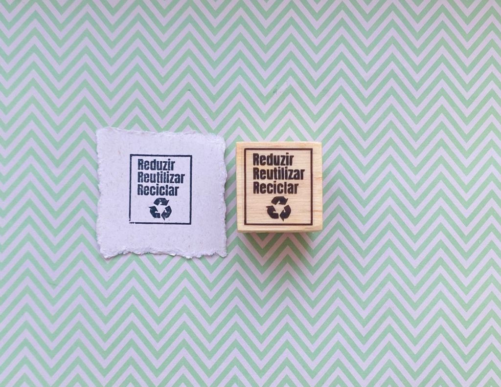 Carimbo de madeira com texto sobre tecido branco e fundo geométrico verde