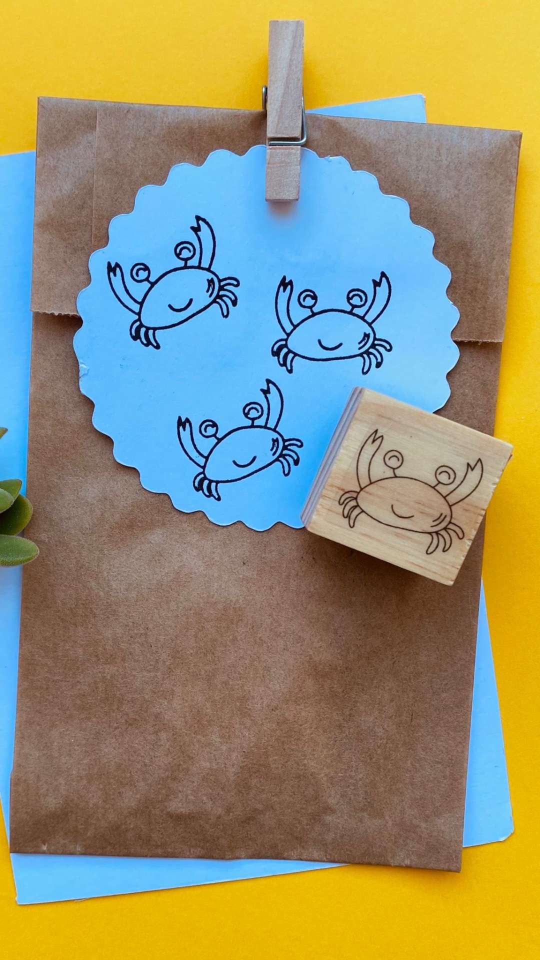 Carimbo de madeira com desenho de caranguejo e impressões em papel azul sobre envelope castanho