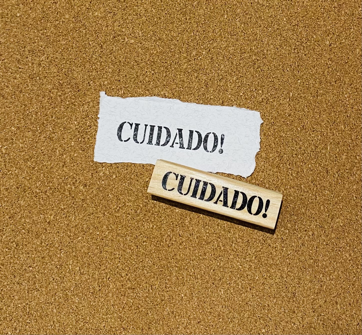Carimbo de madeira com texto CUIDADO e papel branco com o mesmo texto sobre superfície castanha