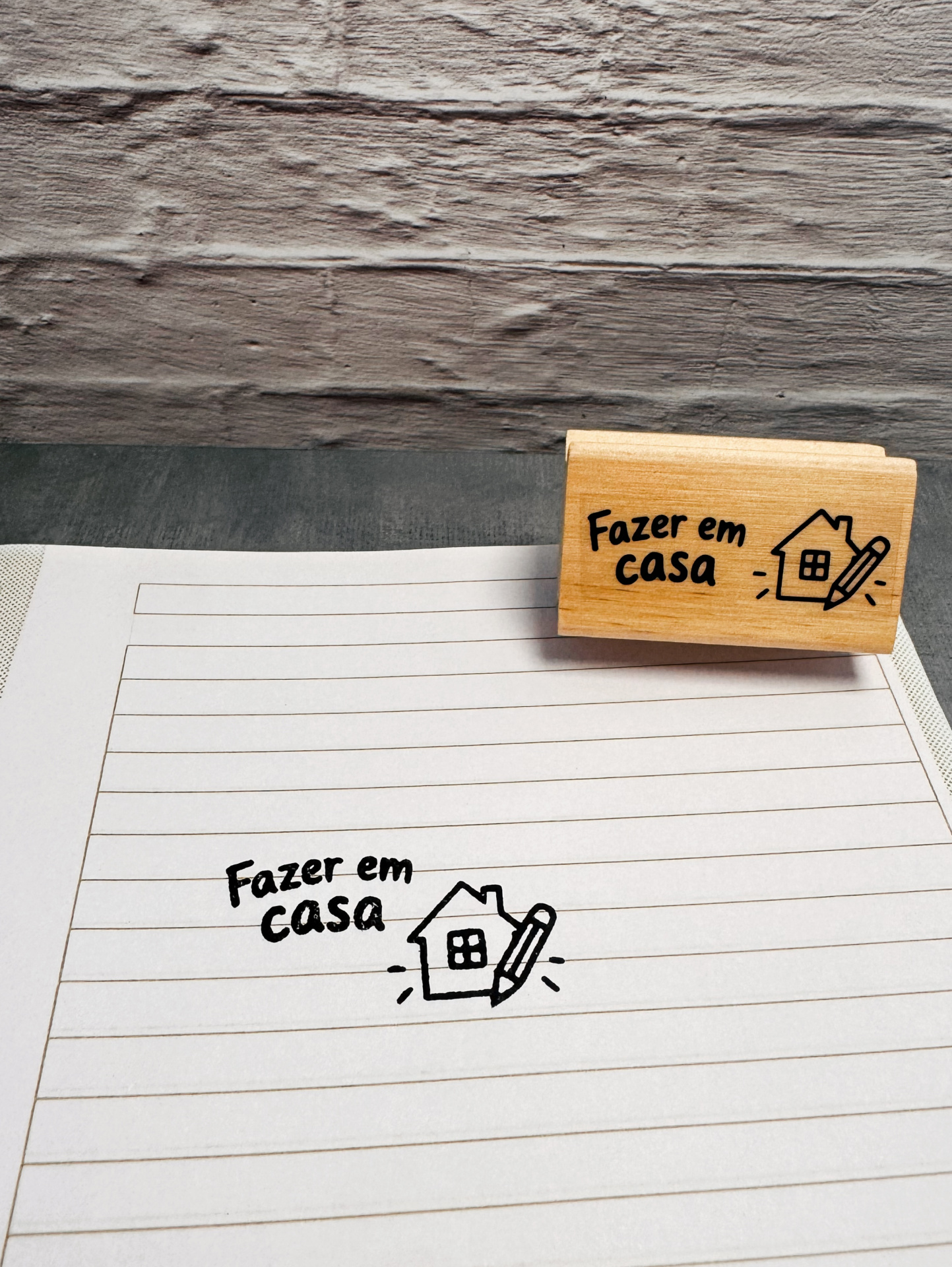 Carimbo de madeira com texto Fazer em casa e desenho de casa com lápis sobre folha pautada