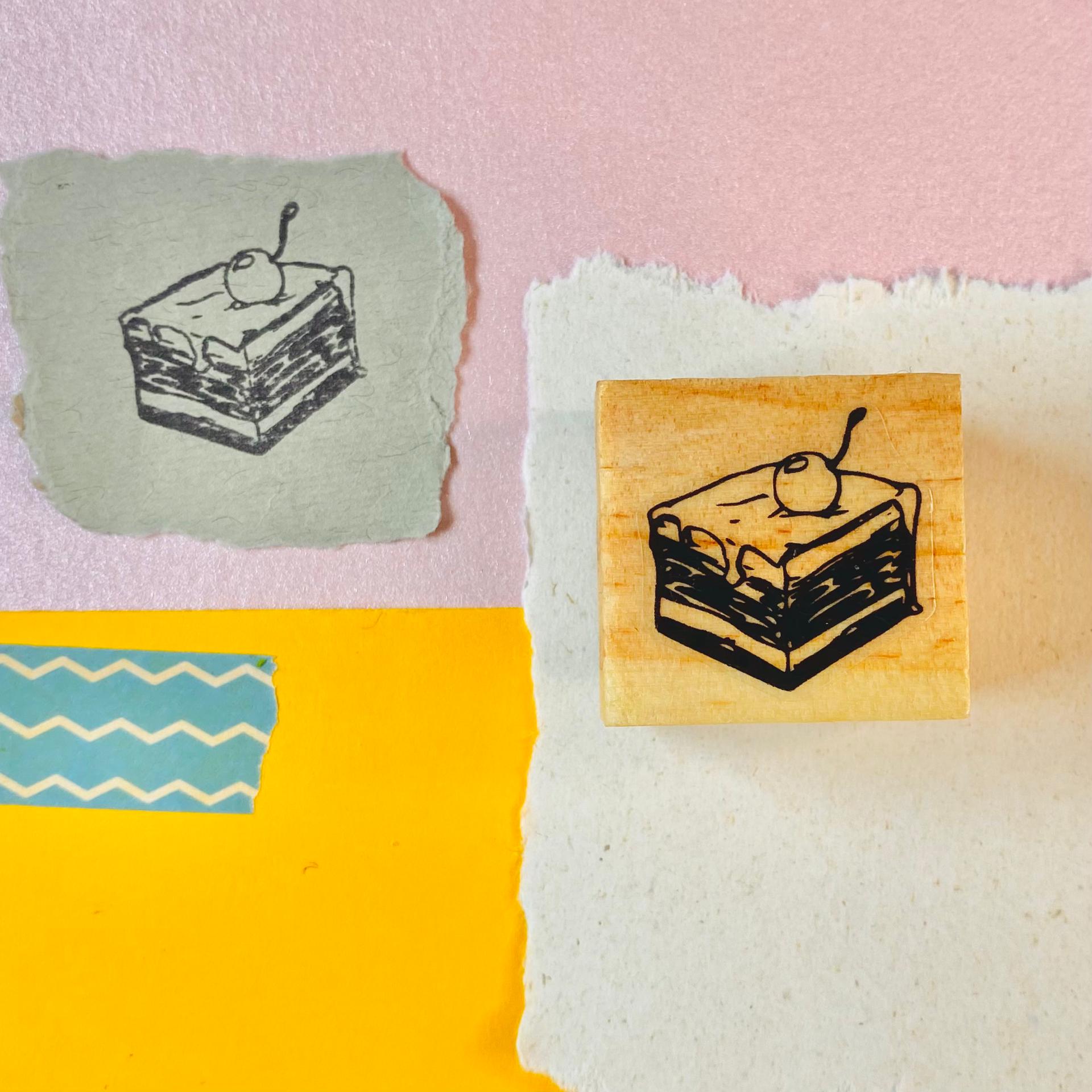 Carimbo de madeira com imagem de fatia de bolo e cereja em papéis coloridos