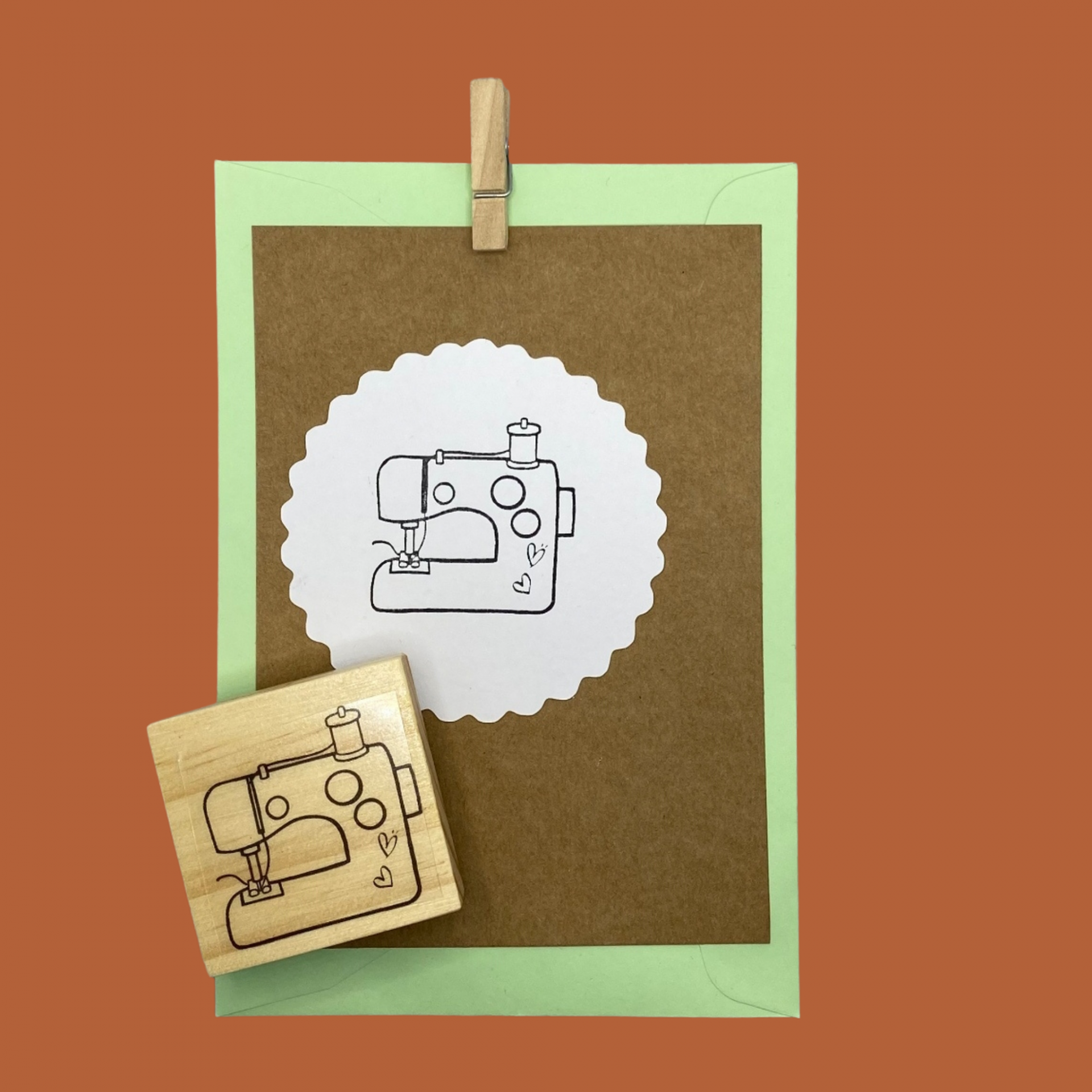 Carimbo de madeira com desenho de máquina de costura sobre cartão castanho e envelope verde