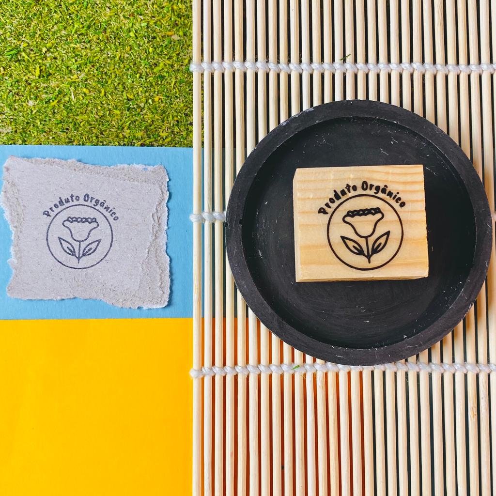 Carimbo de madeira com selo 'Produto Orgânico' e selo impresso em papel sobre fundo colorido