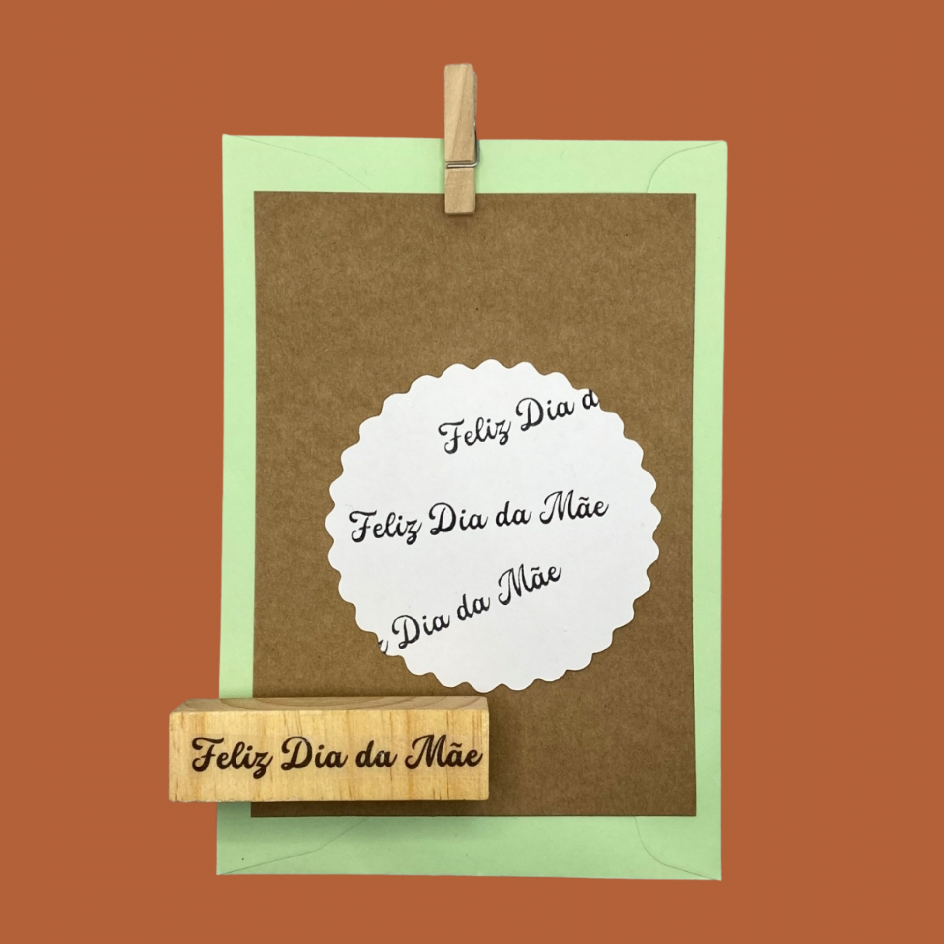 Carimbo e cartão com mensagem Feliz Dia da Mãe, cartão castanho e papel verde com mola de madeira e fundo laranja