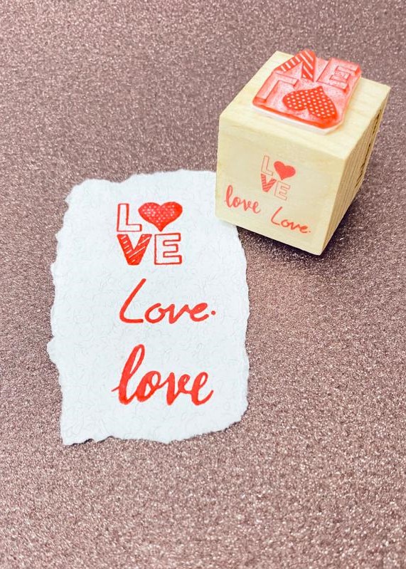 Carimbo de madeira com design 'LOVE' e papel com impressão em vermelho