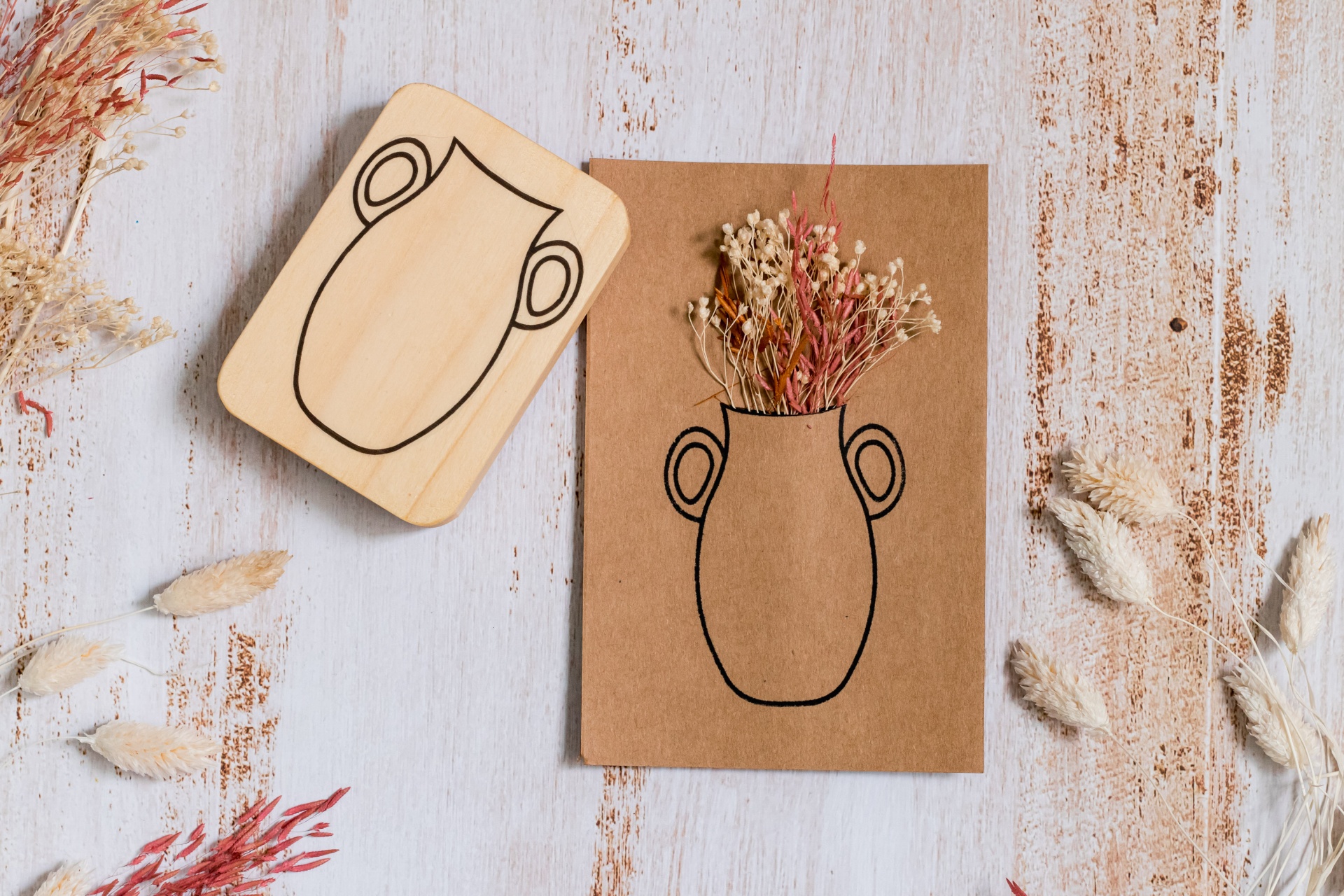Carimbo de madeira com desenho de vaso e cartão castanho com carimbo preenchido por flores secas