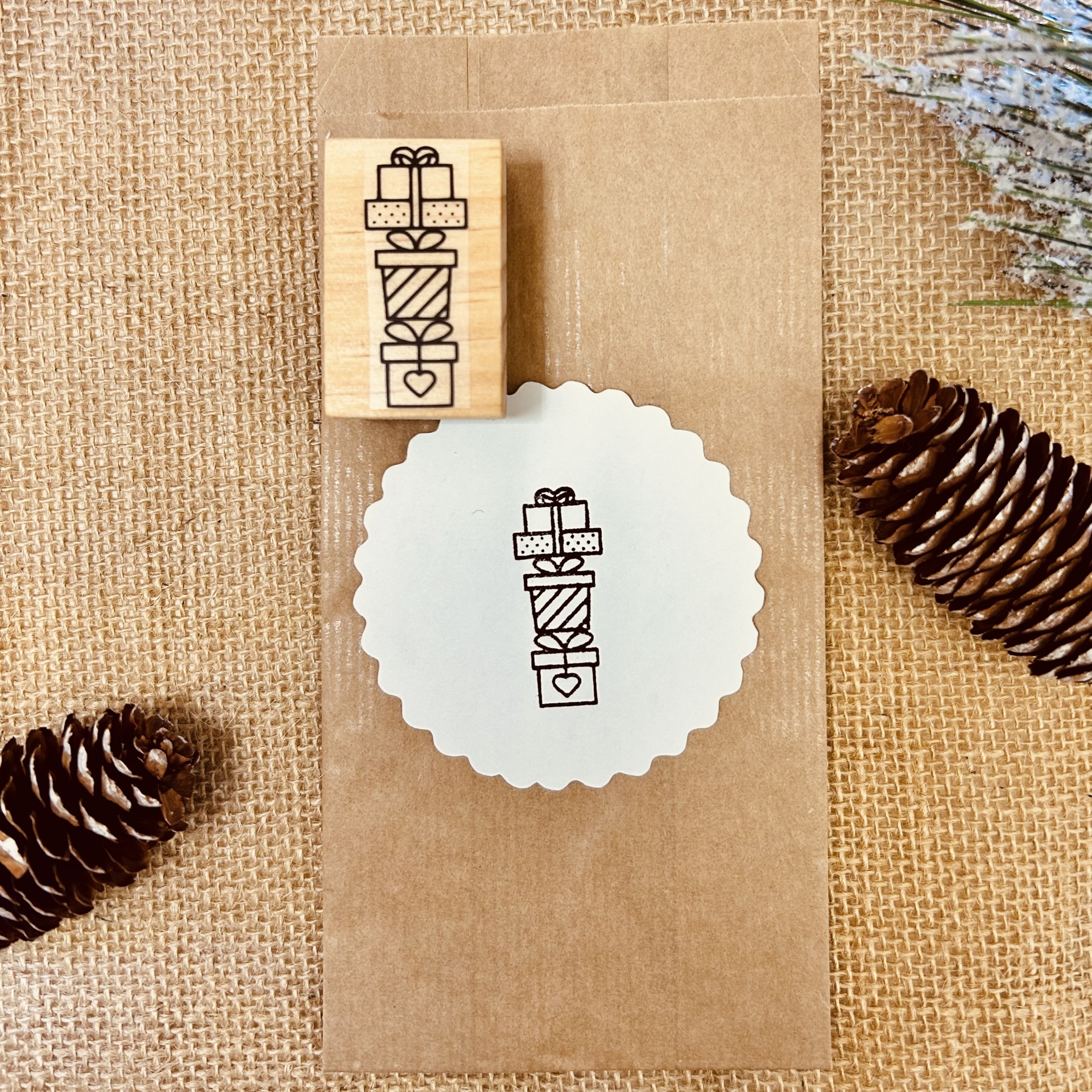 Carimbo de madeira com desenho de presentes e saco em fundo de juta.