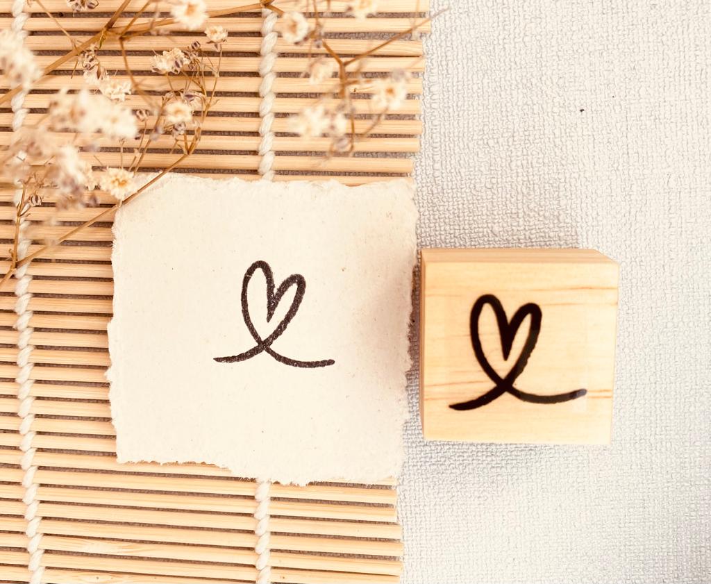 Carimbo de madeira com padrão de coração desenhado em papel sobre tapete de vime e tecido cinzento