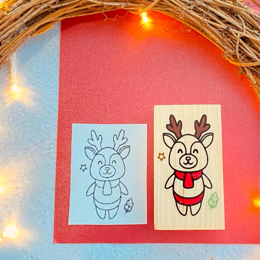 Dois carimbos de madeira com desenho de veado, fundo vermelho e azul, luzes LED e ramos decorativos