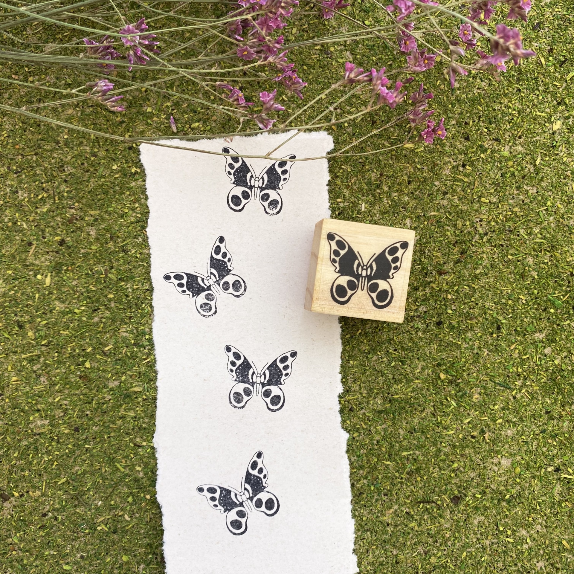 Carimbo de borboleta em madeira e borracha com carimbos pretos em papel branco sobre superfície verde