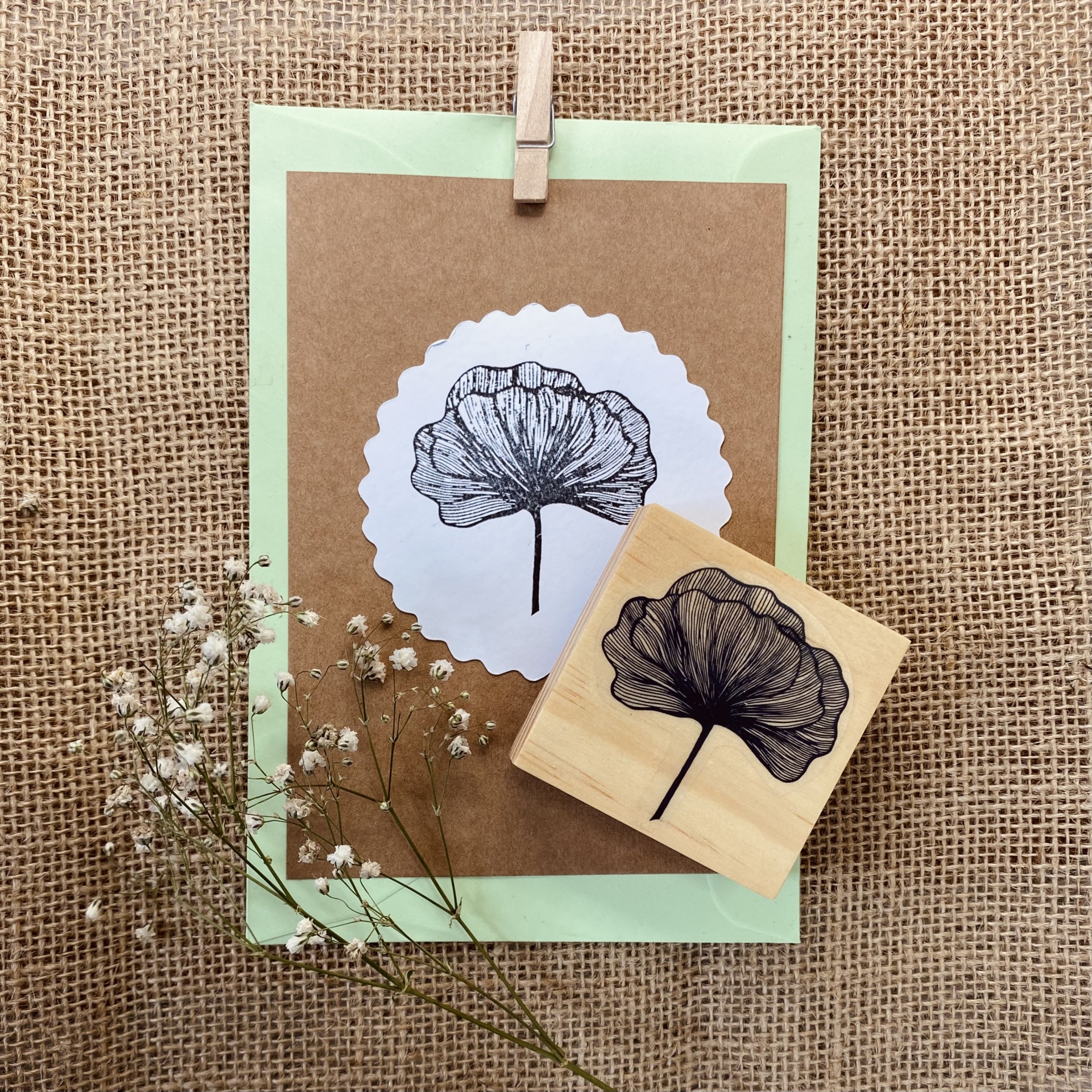 Carimbo de madeira com desenho de folha preta e cartão castanho decorado com a mesma folha em fundo de tecido saco