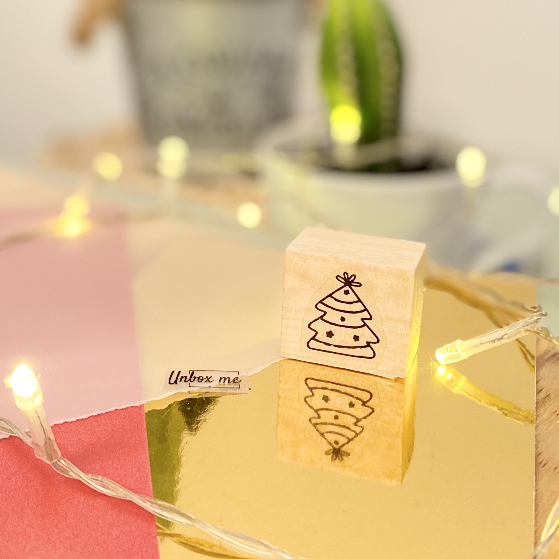 Carimbo de madeira com desenho de árvore de Natal sobre superfície dourada reflexiva e luzes LED