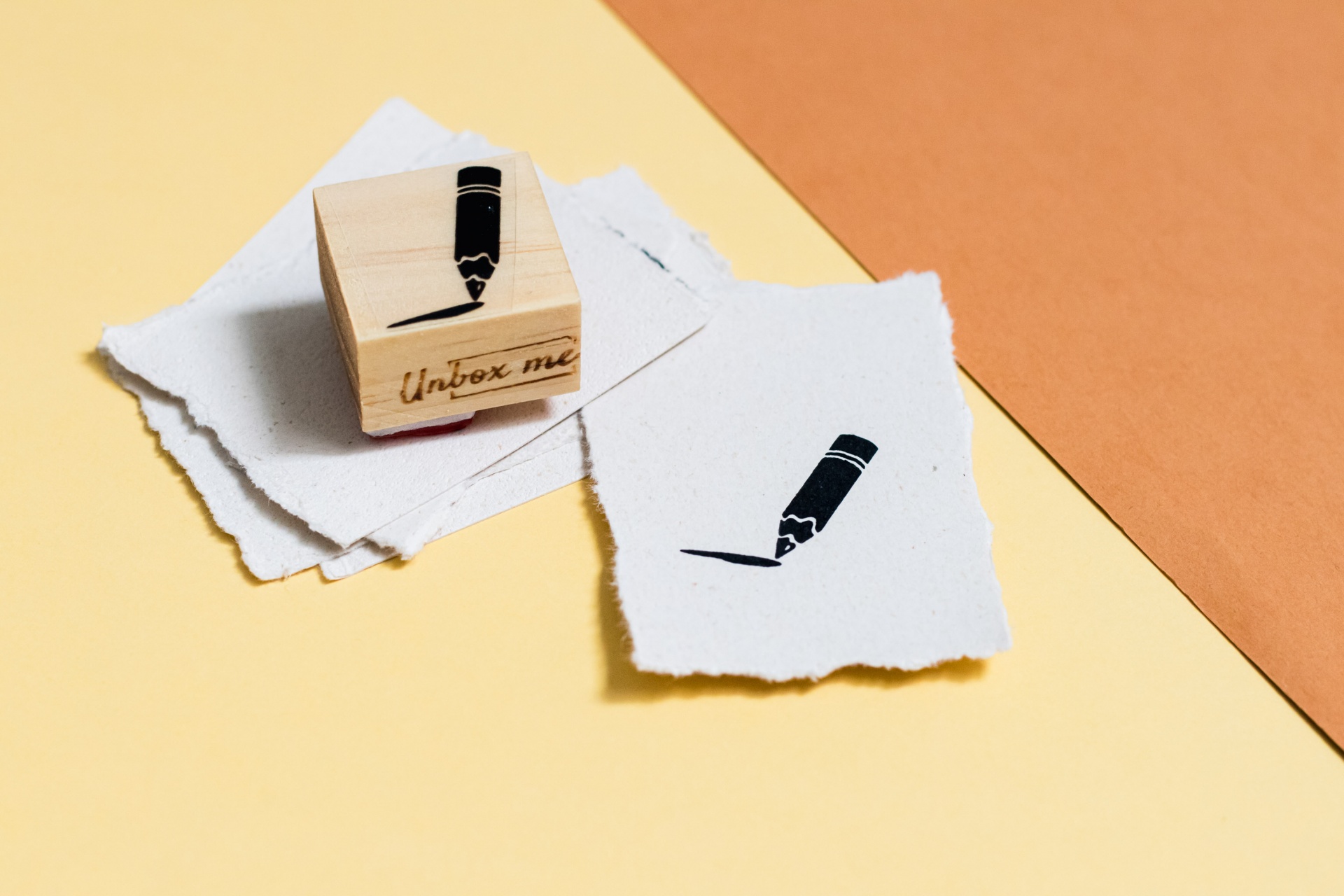 Carimbo de madeira com design de lápis preto e texto 'Unbox me' em papel branco rasgado