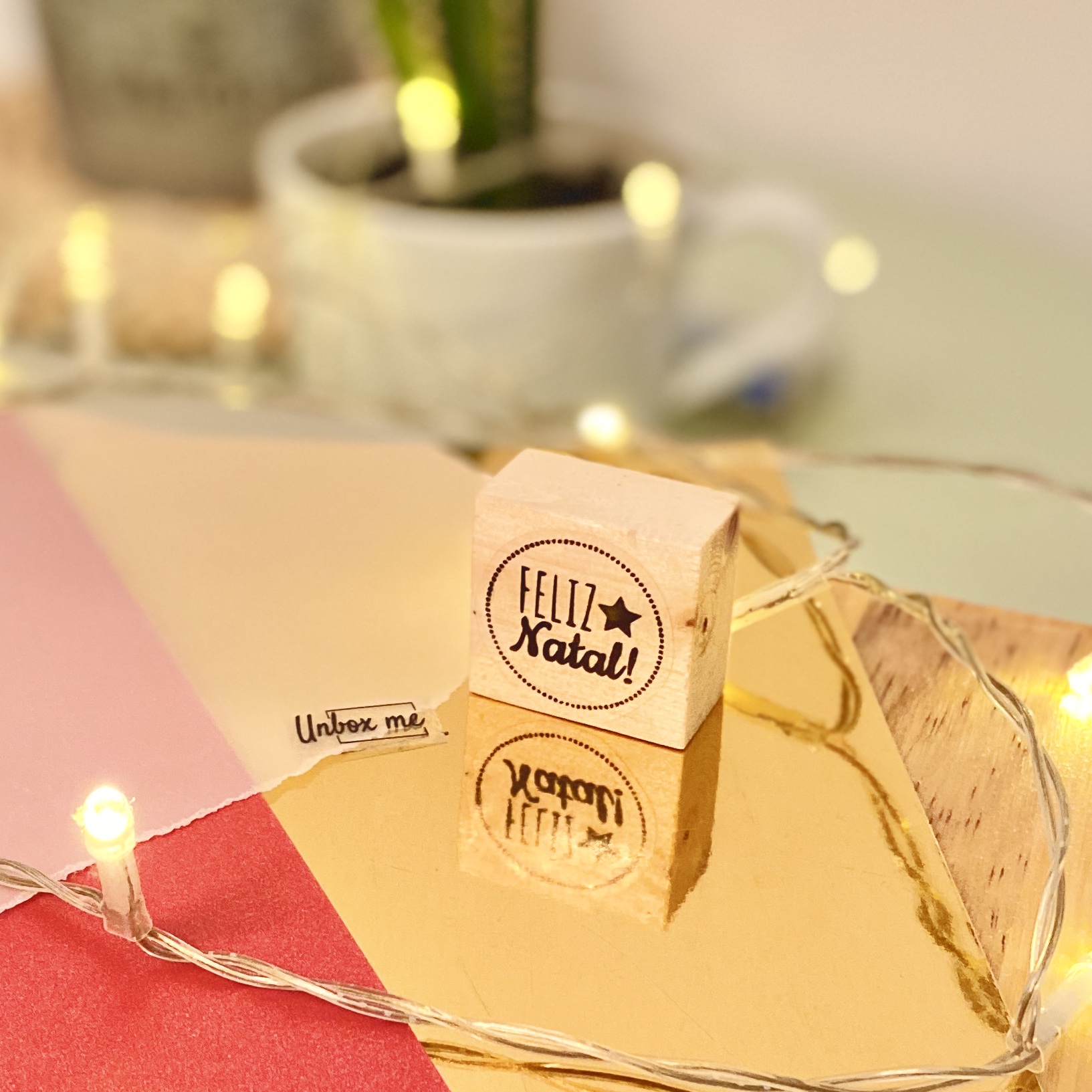 Carimbo de madeira com a inscrição FELIZ Natal! e luzes de fadas em superfície dourada