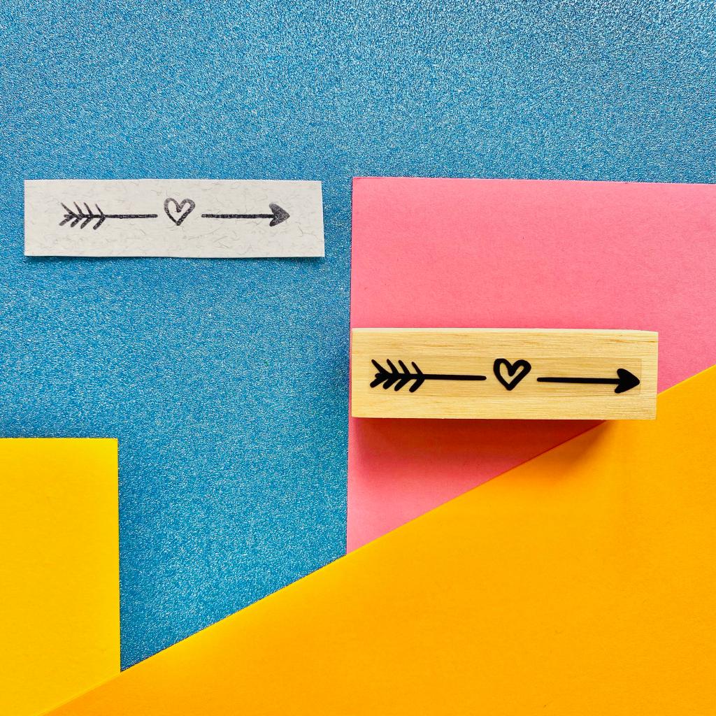Carimbo de madeira com design de flecha e coração e impressão em papel colorido
