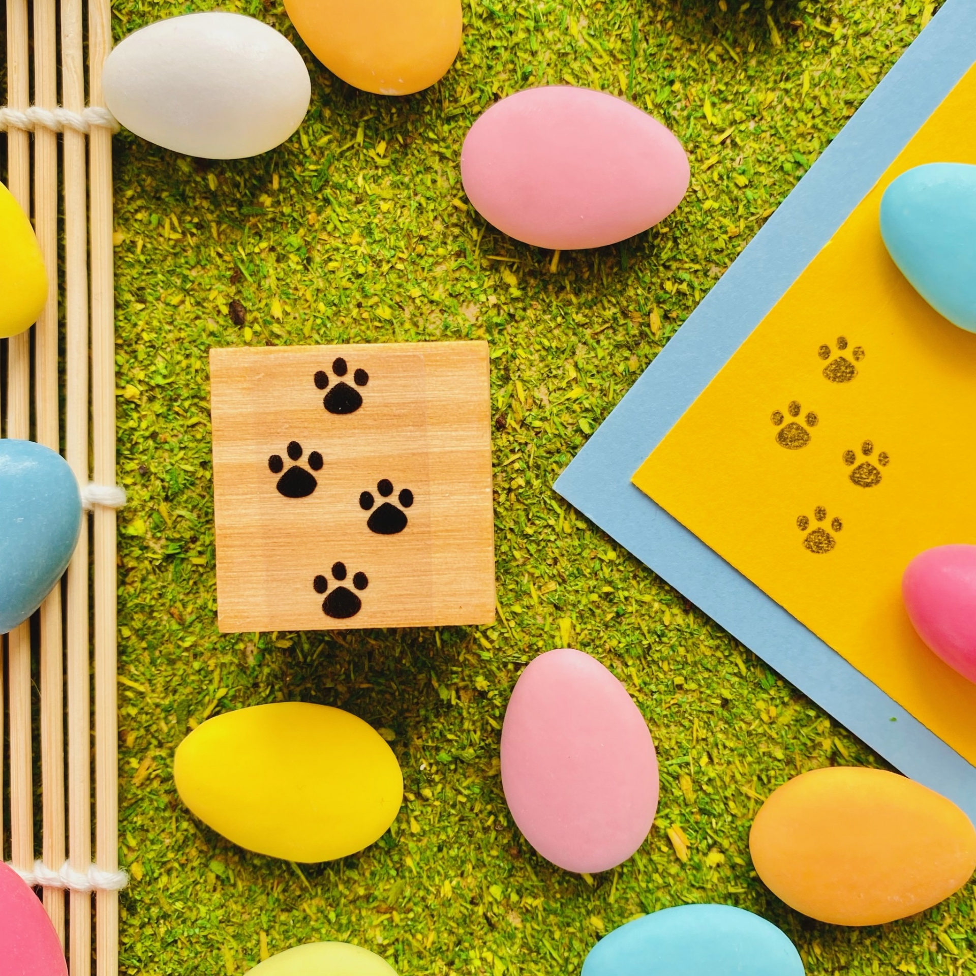 Bloco de madeira com pegadas pretas e ovos coloridos sobre grama