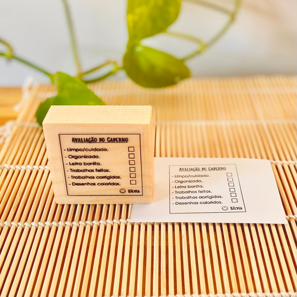 Carimbo de madeira com texto em português e impressão do carimbo num papel branco ao lado, sobre superfície de madeira