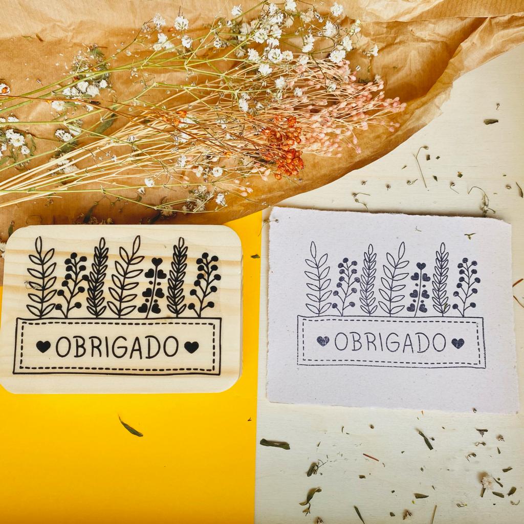 Carimbo de madeira e almofada com desenho de folhas e texto OBRIGADO.