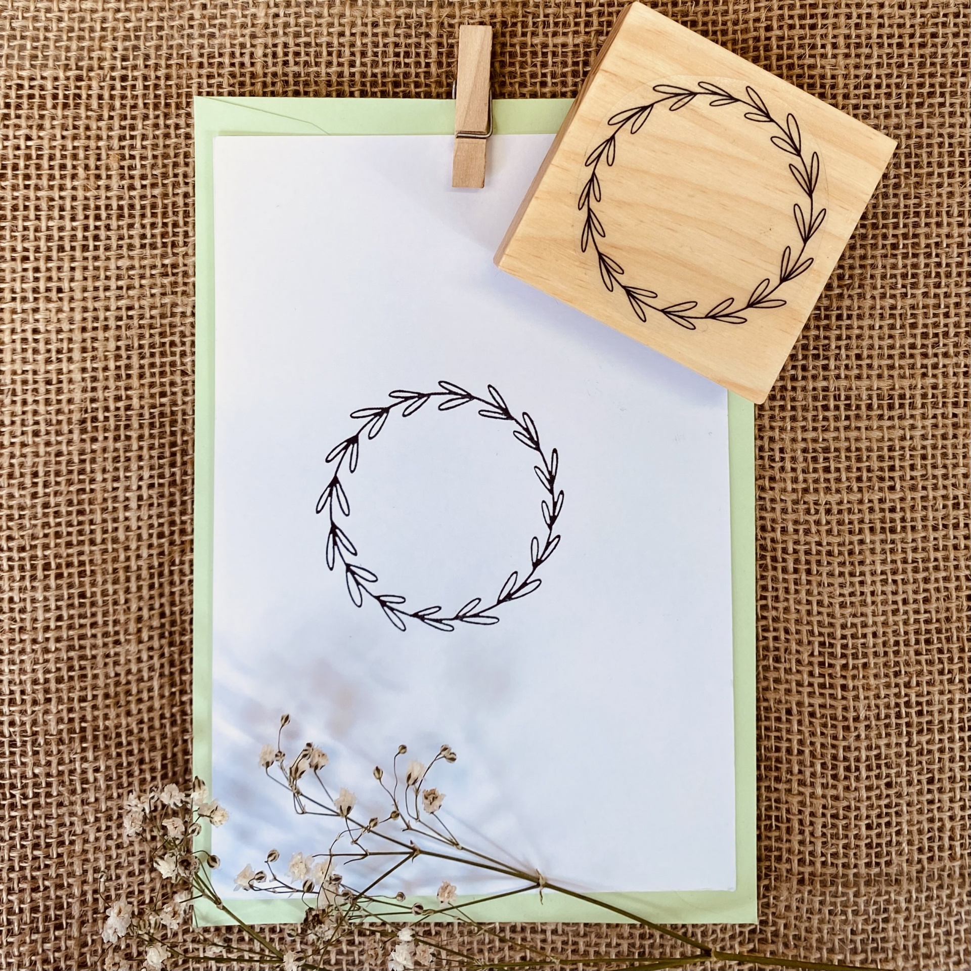 Carimbo de madeira e cartão com padrão de coroa de folhas em fundo de juta